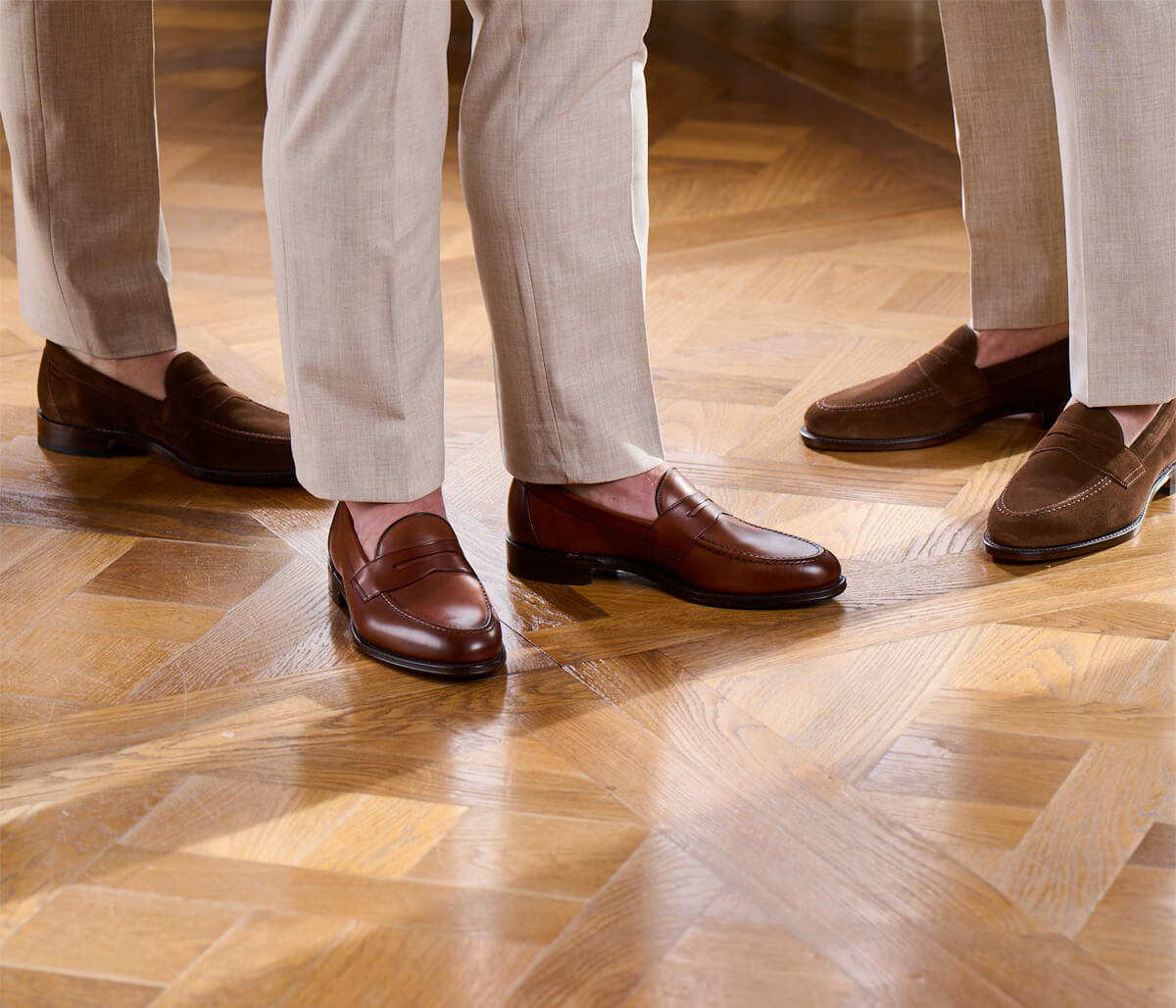 Collection of mens brown loafers in suede and calf leather on wooden flooring with beige trousers